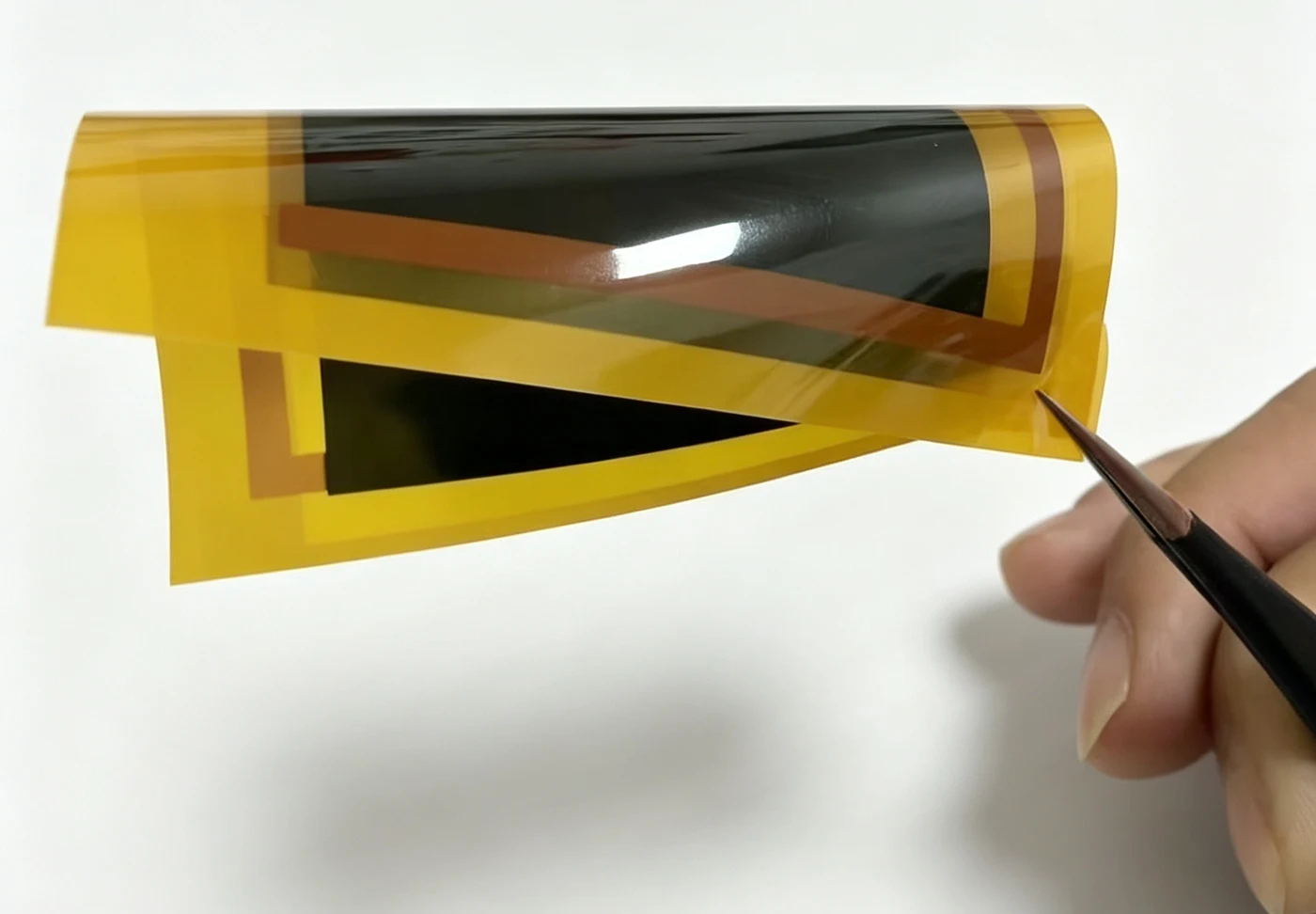 XIHE PI-encapsulated heating-film sample held in a bend, showing the film and copper electrodes